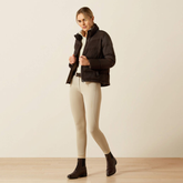 Woman wearing a brown jacket and beige riding breeches against a plain background